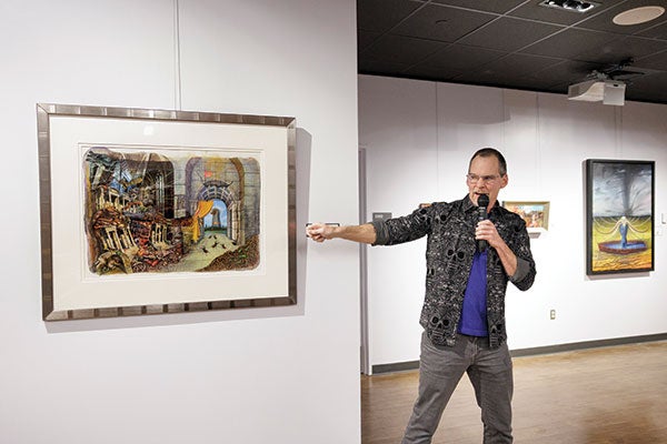 A man with a mic points to a painting.