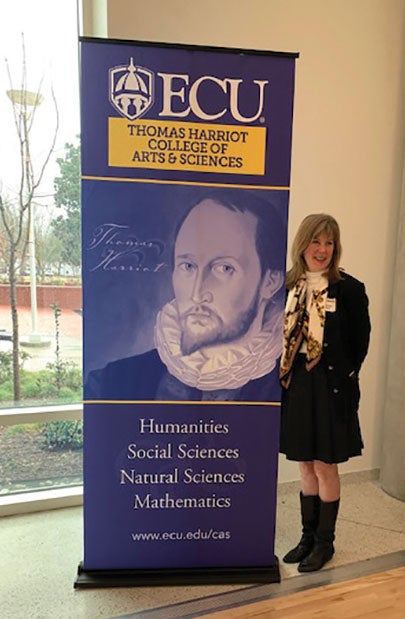 Georgia Dunn Belk poses with a banner showing her ancestor, Thomas Harriot.