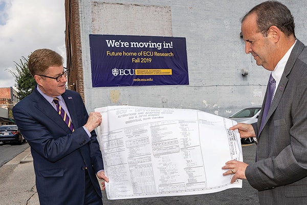 Chancellor Cecil Staton and Jay Golden, vice chancellor for research, economic development and engagement, hold up plans for the refurbishment of the Fifth Street building that will be the new home for ECU research offices.