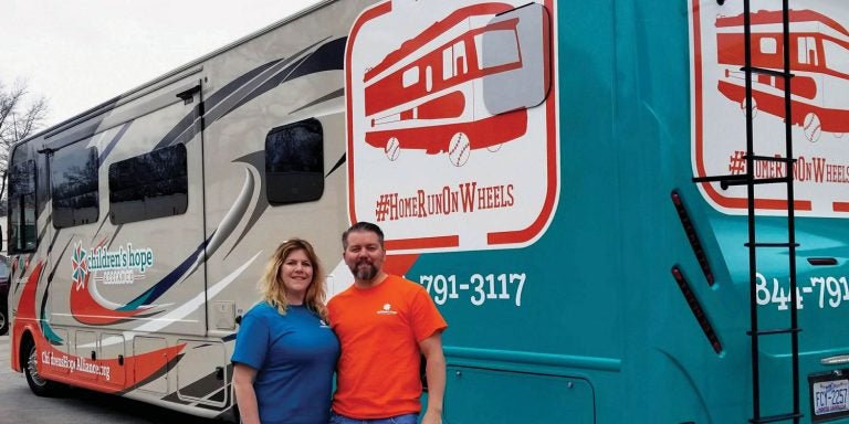 Ron and Patti Clements pose in front of the RV they drove around the country and to Canada, taking foster children to Major League Baseball games.