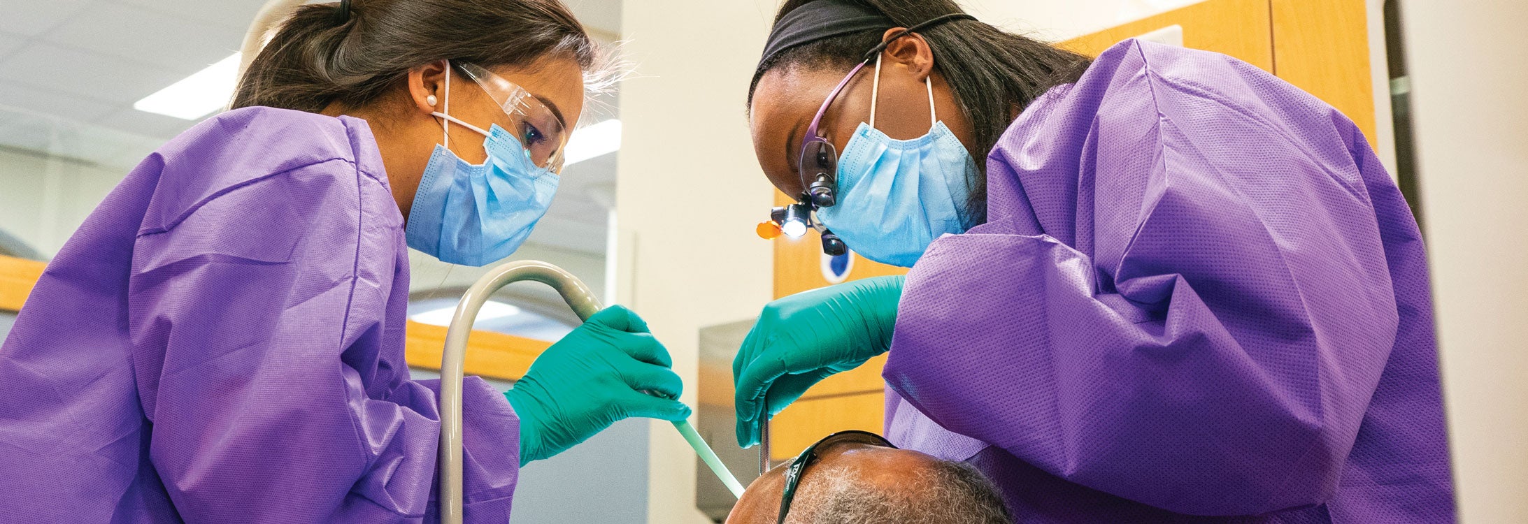 Fourth-year dental students Laura Mercer and Jasmine Schneider work on a patient’s teeth at the Elizabeth City community service learning center.