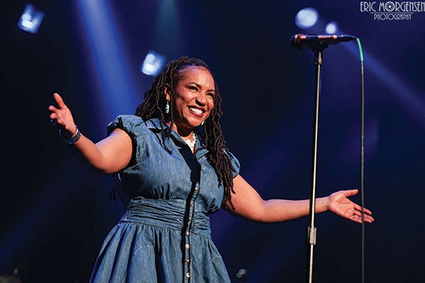 A woman in a blue dress passionately sings into a microphone, captivating her audience with her performance.