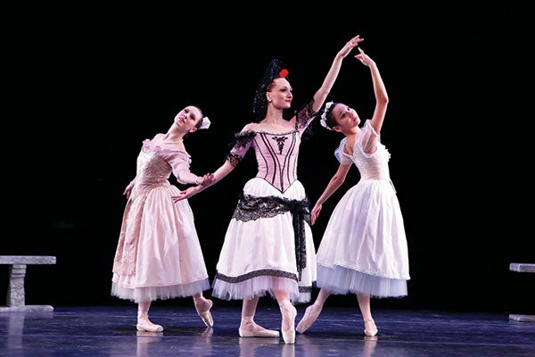 Three ballerinas in elegant tutus and dresses gracefully perform on stage, showcasing their artistry and poise.