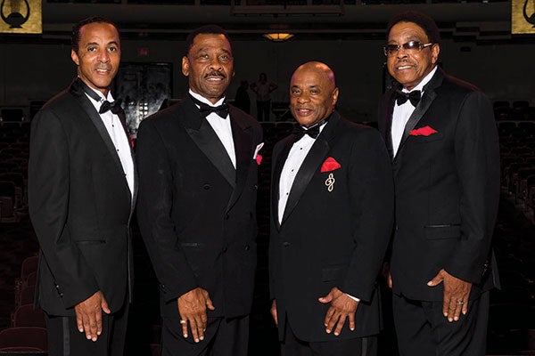 Four men in tuxedos stand together, exuding elegance and camaraderie in a formal setting. 