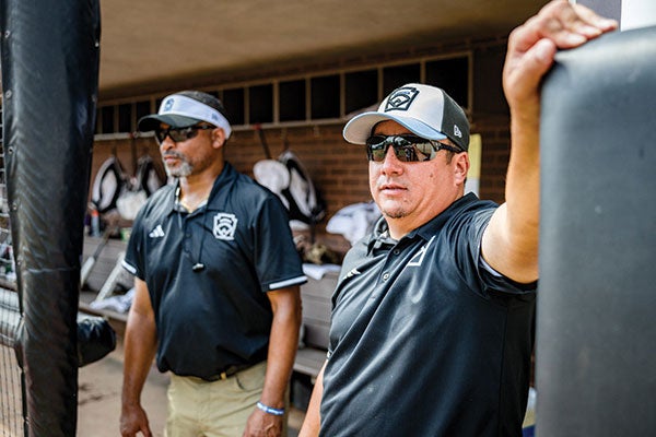 Two men wearing black shirts and sunglasses stand side by side, exuding a cool and confident demeanor.