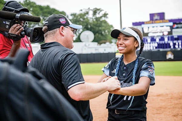 A woman in a baseball uniform shakes hands with a man, symbolizing sportsmanship and teamwork in a friendly encounter.