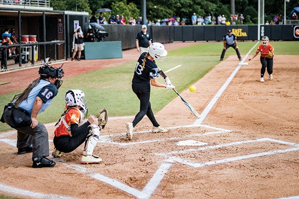 A softball player in action, swinging at a pitch during an intense game on the field.