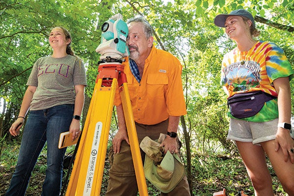 Three people in the jungle use a tripod.