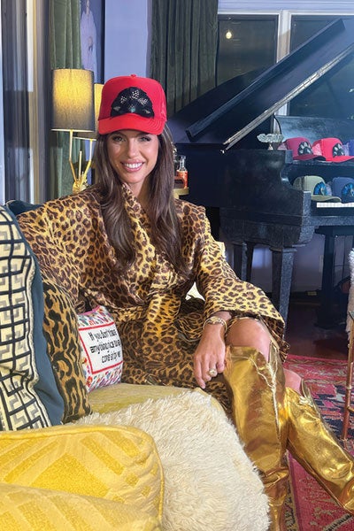 A woman sitting with a red hat and leopard print shirt.