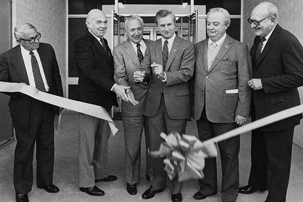 A group of men in suits and ties ceremoniously cutting a ribbon to mark the opening of an event or establishment.