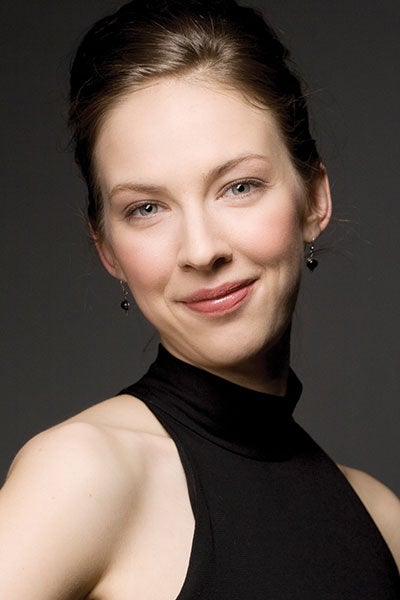 A woman wearing a black top smiles warmly while posing for the camera, exuding confidence and joy. 