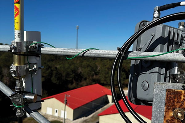 A cell phone antenna mounted atop a tall tower against a clear blue sky, symbolizing modern communication technology.