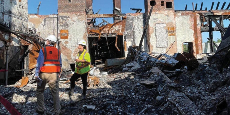 Two men in safety vests assess the debris of a collapsed building, highlighting the aftermath of a structural failure.