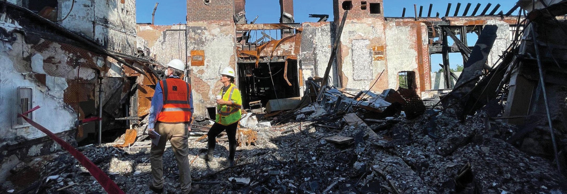 Two men in safety vests assess the debris of a collapsed building, highlighting the aftermath of a structural failure.