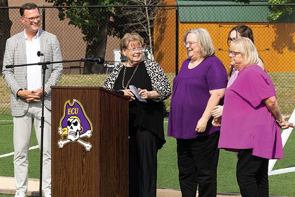 A man and three women listen to a fourth woman give a speech.
