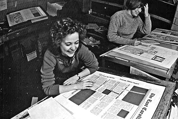 An old photo of students looking over newspapers