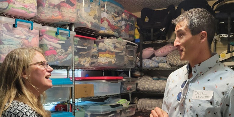 A man and woman stand in a room filled with an assortment of clothes, showcasing a vibrant and diverse wardrobe.