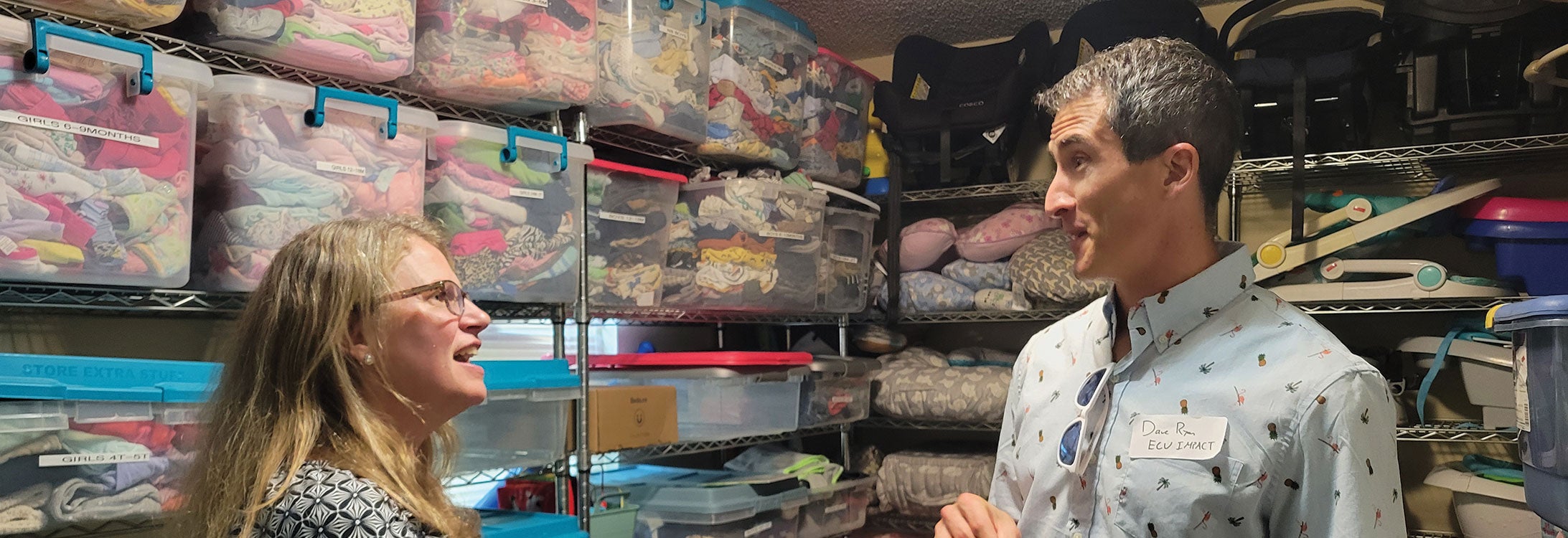 A man and woman stand in a room filled with an assortment of clothes, showcasing a vibrant and diverse wardrobe.