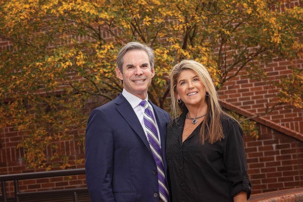 A man and woman stand together in front of a brick building, showcasing a casual yet engaged moment. 