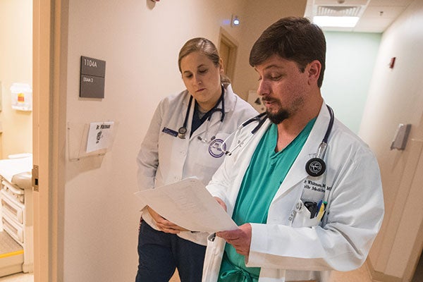 Two doctors in a hallway reviewing a document, engaged in discussion and focused on the paper in their hands.