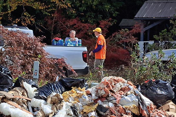 Two men in orange shirts stand beside a large pile of garbage, highlighting the issue of waste management.