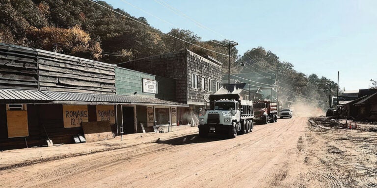 Dump truck drives down a dusty road.