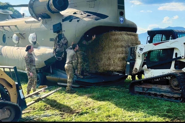 A military personnel loading hay into a helicopter, showcasing a blend of agriculture and aviation in a unique setting.