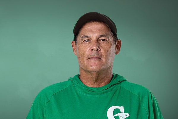 A man dressed in a green shirt and hat, standing confidently with a pleasant expression. 